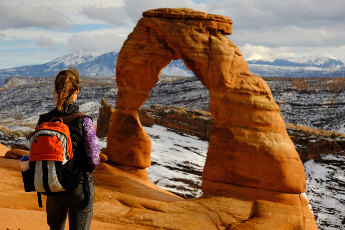 A hiker looks at an arch at Arches National Park