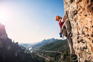 A rock climber on a rock wall with a valley behind him