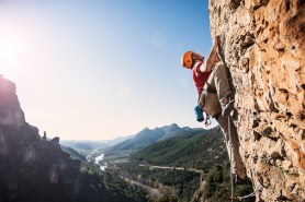 A rock climber on a rock wall with a valley behind him