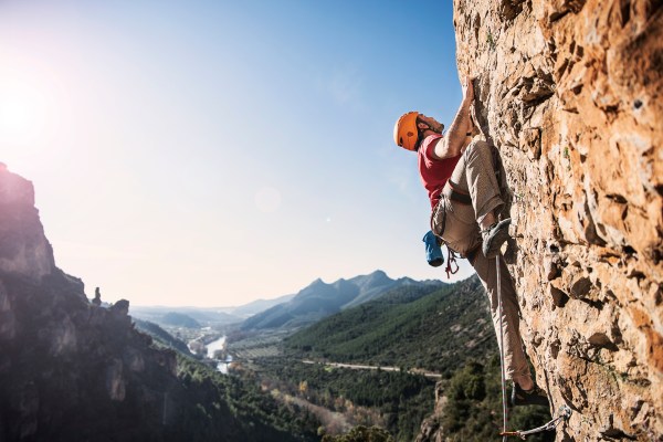A rock climber on a rock wall with a valley behind him